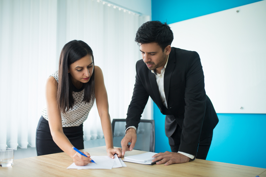 Serious businessman and businesswoman signing contract in boardroom. Young Caucasian female secretary showing papers to executive. Partnership concept